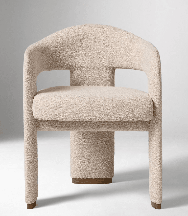 A modern armchair with a rounded backrest and armrests, upholstered in a textured boucle fabric. The chair features a substantial, cylindrical pedestal base with a subtle wood accent at the bottom, and two thick, curved legs extending from the sides of the seat. The overall design is sculptural and contemporary. — 3D model