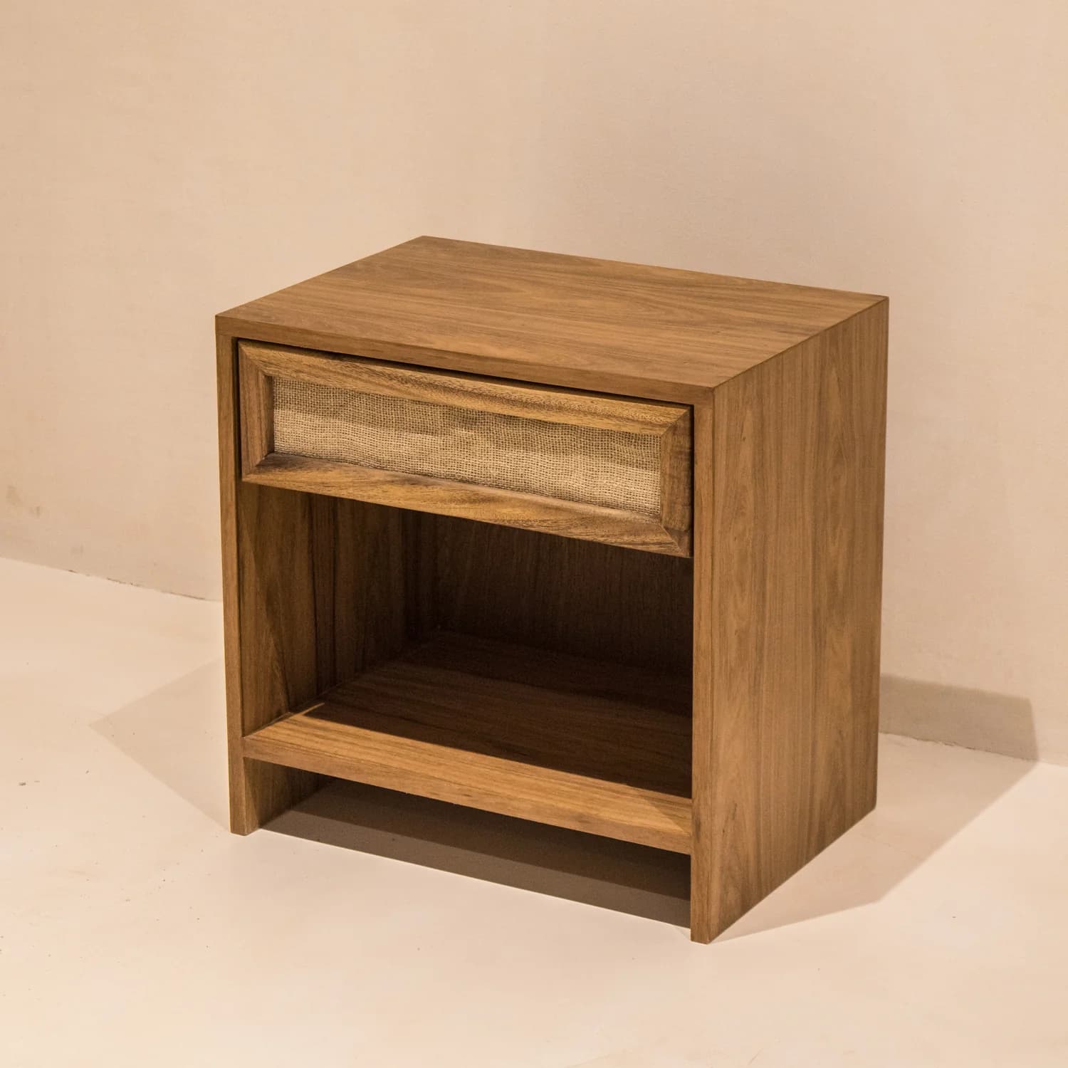 A modern wooden nightstand featuring a single top drawer with a woven rattan or cane panel insert, positioned above an open storage cubby. The piece is crafted from medium-toned wood, showcasing a natural grain, and stands on a recessed plinth base. — 3D model