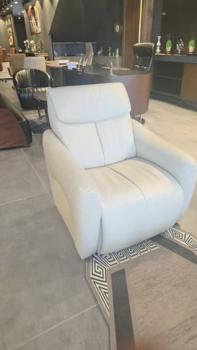 A modern, generously upholstered armchair in a light cream or off-white color. It features soft, rounded forms, wide padded armrests, and a plush backrest with an integrated headrest, suggesting comfort and relaxation. — 3D model