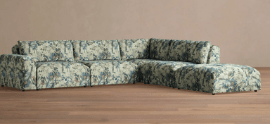 A sectional sofa with a corner chaise lounge. The sofa features a densely patterned upholstery with a botanical motif in shades of blue, green, and beige. It has a low profile with visible dark feet. — 3D model