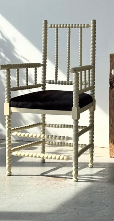 A white painted wooden armchair featuring distinctive spool-turned legs, stretchers, armrests, and backrest spindles. It is fitted with a contrasting black upholstered seat cushion. — 3D model