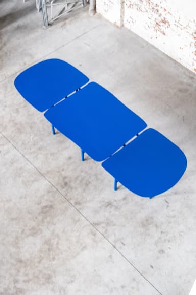A long, modular dining table featuring three distinct segments with rounded ends, supported by a vibrant blue tubular metal frame. Each segment's top is dark blue, complementing the bright blue base, with small green connectors and feet accents. — 3D model