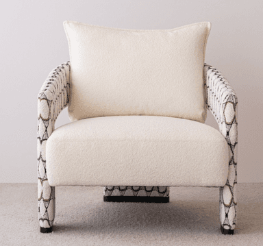 A contemporary upholstered armchair featuring a plush, light-colored bouclé fabric on the seat and back, complemented by patterned armrests and legs with a geometric design in black, white, and a coppery tone. It includes a matching back cushion. — 3D model