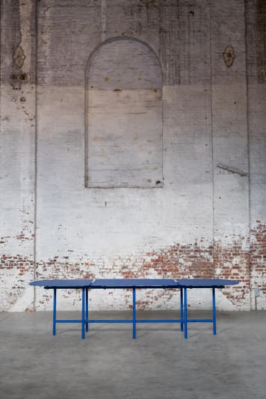 A long, modular dining table featuring three distinct segments with rounded ends, supported by a vibrant blue tubular metal frame. Each segment's top is dark blue, complementing the bright blue base, with small green connectors and feet accents. — 3D model