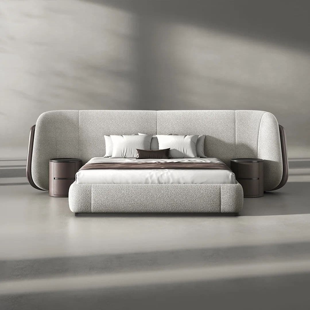 A modern, upholstered platform bed featuring an expansive, curved headboard with vertical channel stitching. The headboard seamlessly integrates two circular, dark wood nightstands on either side, each with two drawers. The bed frame itself is also upholstered in a light grey textured fabric, resting on a subtle, dark base. The bed is adorned with white and brown bedding. — 3D model