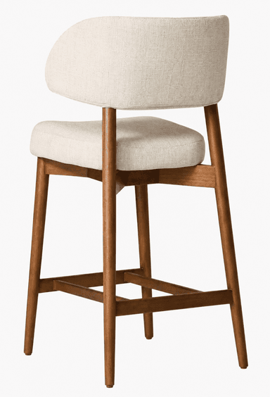An upholstered counter stool featuring a natural wood frame and an off-white fabric seat and backrest. The design incorporates mid-century modern aesthetics with splayed legs and a curved, supportive backrest. A footrest is integrated into the lower part of the frame. — 3D model