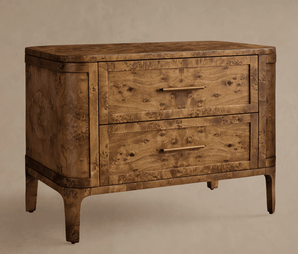 A compact two-drawer nightstand or side cabinet crafted from burl wood veneer, featuring a rich, intricate grain pattern. The piece has soft, rounded corners on its top and sides, and the base flows seamlessly into four short, tapered legs. It is equipped with two full-width drawers, each fitted with a slender, rectangular brass or bronze bar pull handle. — 3D model