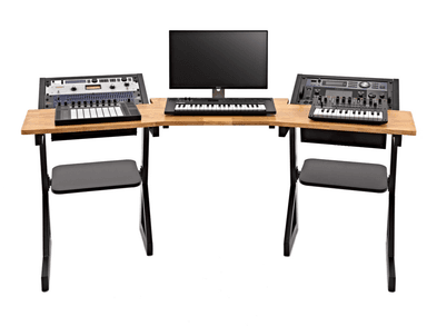 A long, ergonomic studio desk designed for audio production. The desk features a natural wood-finished desktop with a gently curved front edge. It has a modular design with angled black metal legs and integrated shelves beneath the main surface. The desk is equipped with several pieces of audio equipment, including a monitor, a mixing console, and multiple keyboard controllers. — 3D model