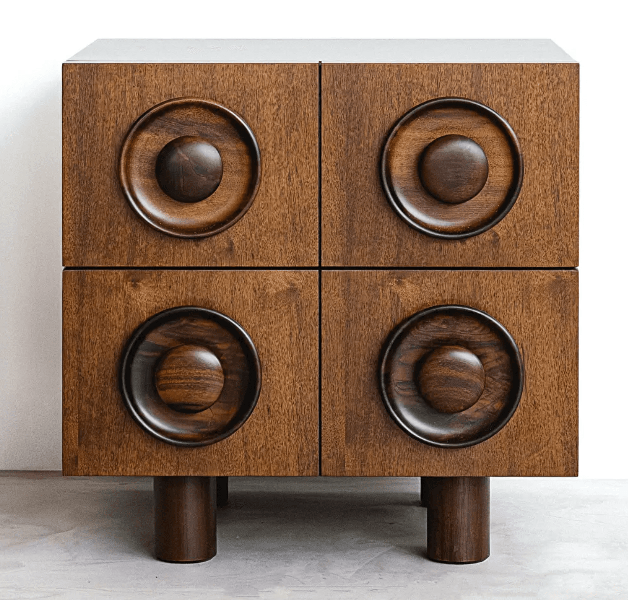 A compact, rectangular wooden cabinet featuring a dark stained finish and distinctive sculptural circular handles on each of its four front panels. The cabinet stands on four robust cylindrical legs, and its top surface appears to be a lighter, contrasting material. The design is notably geometric and tactile. — 3D model