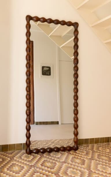 A decorative mirror with an irregularly shaped frame, featuring a repeating bobble or bead pattern along its edge. The frame is made of dark wood and has a somewhat organic, curved silhouette. The reflective surface is rectangular, with a slightly distorted perspective due to the angle of the object. — 3D model