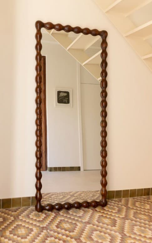 A decorative mirror with an irregularly shaped frame, featuring a repeating bobble or bead pattern along its edge. The frame is made of dark wood and has a somewhat organic, curved silhouette. The reflective surface is rectangular, with a slightly distorted perspective due to the angle of the object. — 3D model
