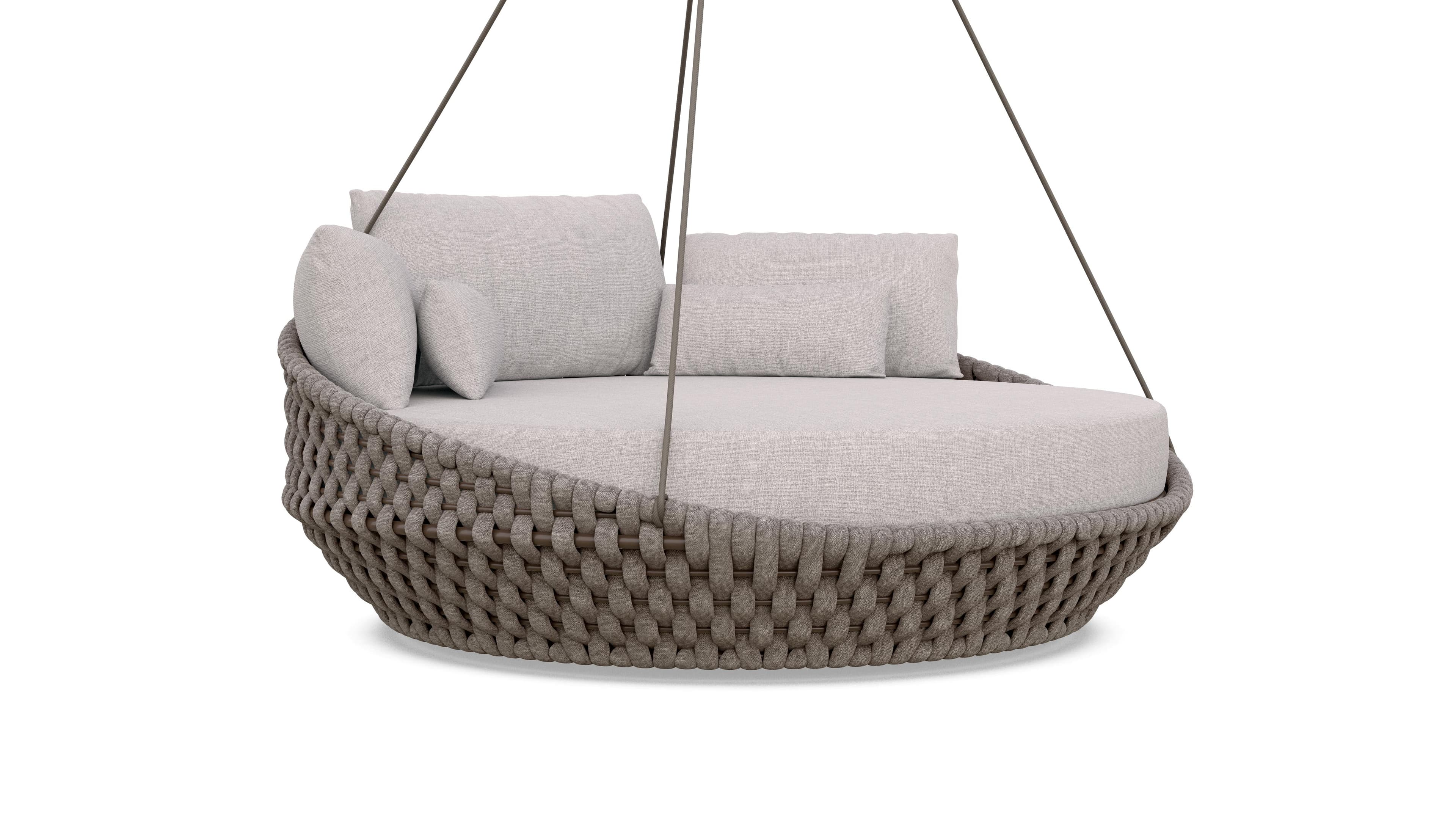 A contemporary hanging daybed designed for outdoor or indoor use. The circular seating area is upholstered in a light-colored, textured fabric. The base is constructed from a woven rope or cord material over a frame, giving it a natural and airy aesthetic. It is suspended by thin, dark-colored cables, suggesting it is designed to hang from a support structure. Several plush cushions in a matching fabric provide comfort and support. — 3D model