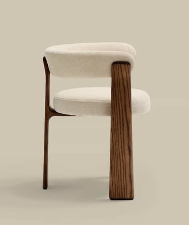A modern armchair featuring a sculpted dark wood frame and cream-colored textile upholstery. The chair has a rounded, continuous backrest and armrests, and a circular seat cushion. The robust, splayed wooden legs provide a stable and aesthetically integrated base. — 3D model