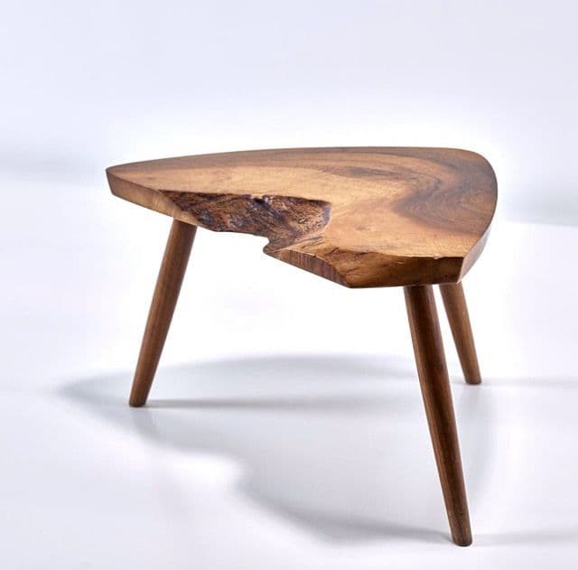 A small, irregularly shaped end table with a live-edge wooden top and three tapered wooden legs. The tabletop exhibits natural wood grain and a rough, unfinished edge on one side. The legs are angled and extend from beneath the tabletop. — 3D model