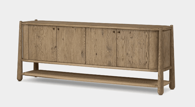 A rustic light oak sideboard featuring four cabinet doors with exposed wood grain and small black knob handles. The main cabinet rests on an elevated frame that extends to form the legs, with a woven cane shelf integrated into the lower structure. The wood has a natural, slightly weathered finish and rounded edges. — 3D model