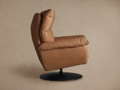A contemporary armchair upholstered in tan leather, featuring a plush, segmented backrest and seat, rounded armrests, and a circular swivel base in black metal. The design emphasizes comfort with its soft, yielding upholstery and supportive structure. — 3D model