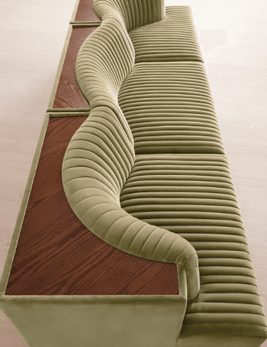 A contemporary sofa upholstered in a rich green velvet, featuring distinctive channel tufting across its backrest and seat. The sofa integrates a continuous wooden surface that serves as armrests and a functional back shelf, with sculpted cut-outs that conform to the upholstered backrest. — 3D model
