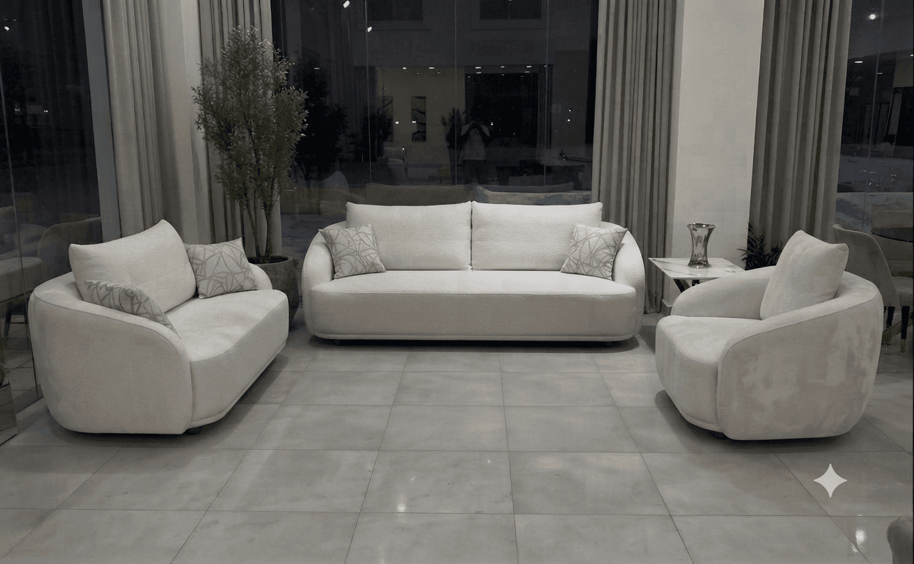 A modern, light beige three-seater sofa with a distinctive curved silhouette, upholstered in a subtly textured fabric, featuring three seat cushions, two back cushions, and two patterned throw pillows. — 3D model