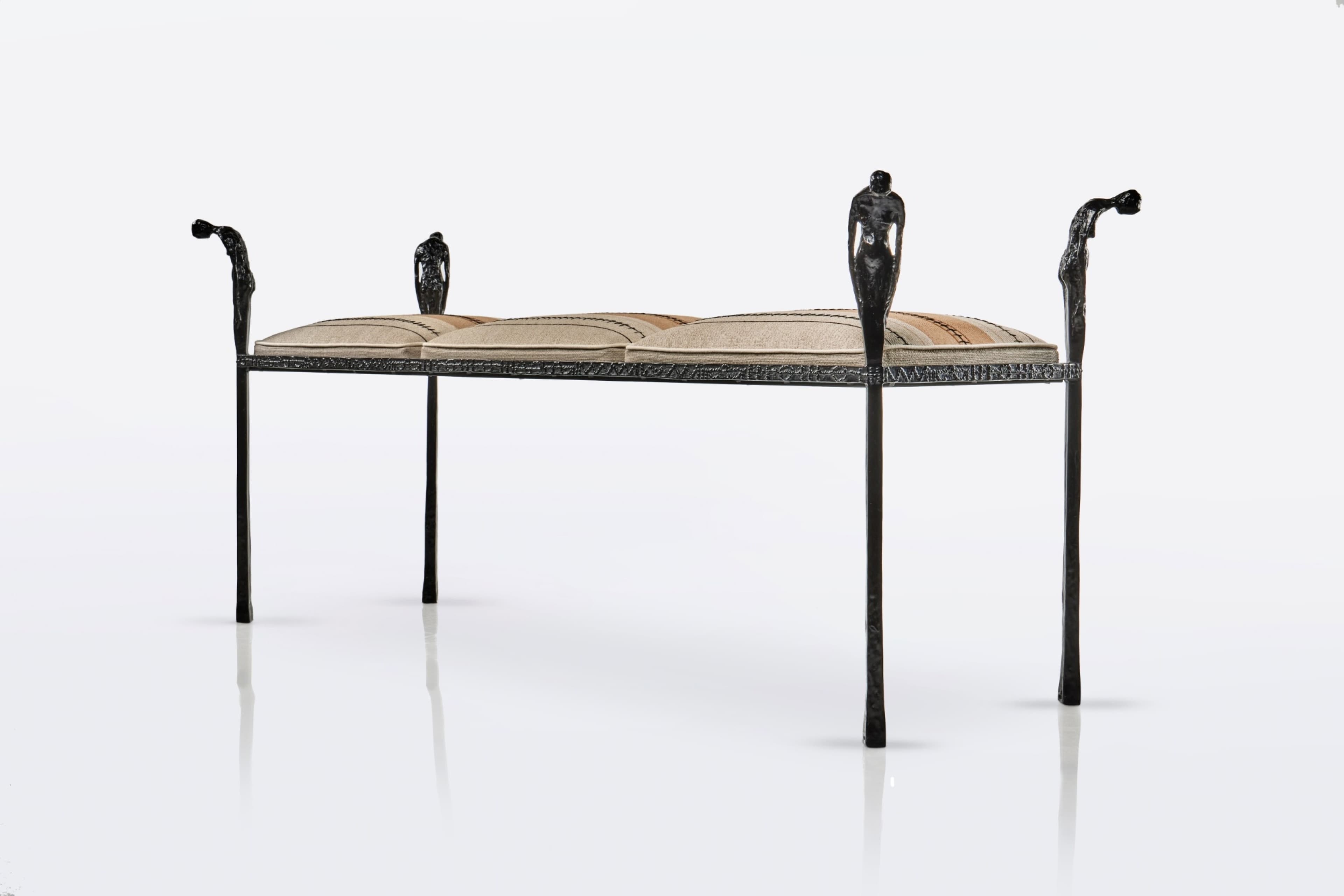 A distinctive figural wrought iron bench featuring a dark, textured metal frame with decorative uprights sculpted as human figures, supporting segmented upholstered cushions with a striped pattern. The bench has four slender legs and decorative arm-like elements at each end, also featuring figural motifs. — 3D model