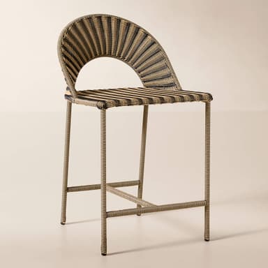 A close-up image of a contemporary accent chair constructed from two-tone synthetic rattan. The chair features a tightly woven pattern in alternating bands of black and light beige, creating a striped effect. It has a curved backrest and integrated armrests, suggesting a comfortable, ergonomic form. The legs, visible at the bottom, also appear to be wrapped in the same woven material, indicating a cohesive design. The texture is smooth and uniform, characteristic of synthetic materials. — 3D model