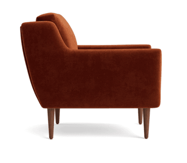 A contemporary armchair upholstered in a rich burnt orange velvet fabric. It features a boxy silhouette with slightly angled, wide arms that flow into the backrest. The armchair has a loose seat cushion and a separate back cushion, both generously padded. It stands on four slender, tapered wooden legs with a medium-dark finish. The design suggests a blend of modern and mid-century aesthetics. — 3D model