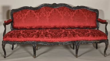 A vintage-style sofa with a carved wooden frame and upholstered seating and backrest. The frame exhibits ornate detailing, painted in a dark color, likely black or dark brown, with some gilded accents visible. The upholstery is a deep red fabric with a damask pattern, covering the seat, back, and armrests. The sofa features cabriole legs and curved armrests typical of Baroque or Rococo design influences. — 3D model