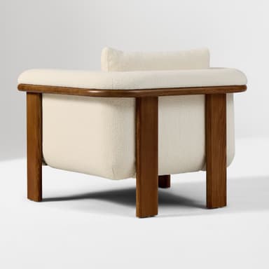 A contemporary armchair featuring a solid wood frame with natural wood grain visible. The seating and backrest are upholstered in a textured, light-colored fabric. The design incorporates a rounded aesthetic with distinct block-style wooden legs and integrated armrests that extend from the frame. — 3D model