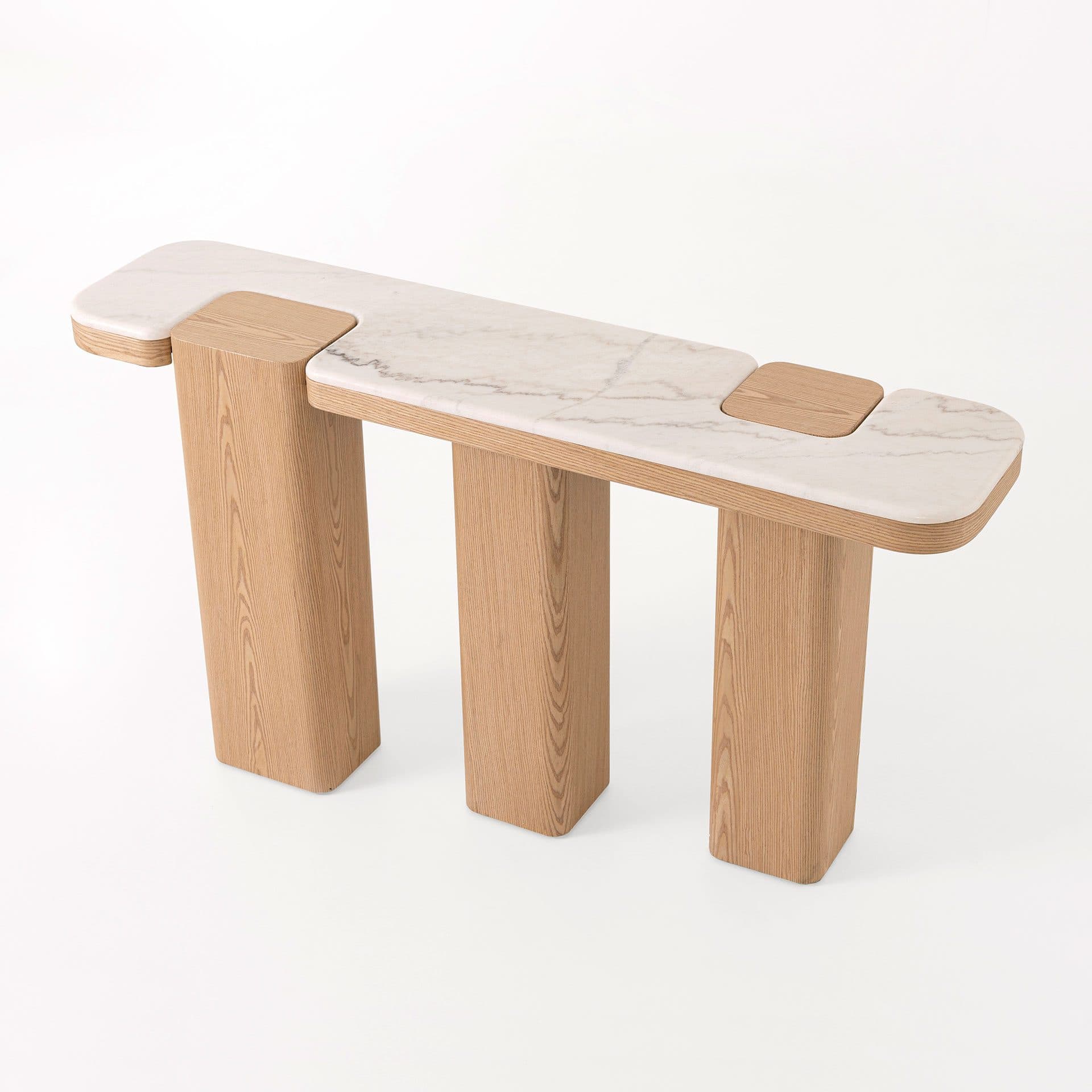 A modern console table with a distinctive design. It features a rectangular top made of white marble with subtle grey veining, supported by three thick, rounded wooden legs. The marble top is segmented, with two distinct wooden inlays that are flush with the surface, creating a unique visual texture. The legs are solid and have a natural wood grain finish. The overall aesthetic is minimalist and sculptural. — 3D model