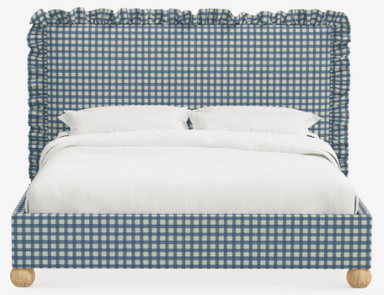 A bed featuring an upholstered headboard and frame in a blue and white gingham fabric. The headboard is designed with a distinctive ruffled trim along its top and side edges. The bed frame is supported by four spherical light-toned wooden feet. White bedding, including pillows and a duvet, is present on the bed. — 3D model