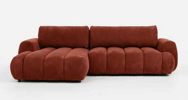 A modern sectional sofa featuring a distinct channel-tufted design in a rich terracotta-colored fabric. The sofa consists of at least two modular sections, forming an L-shape with a chaise component. Its form is characterized by soft, rounded edges and horizontal channeling across the seat, back, and armrests, giving it a plush, voluminous appearance. The fabric appears to be a textured, perhaps bouclé or chenille, adding to its inviting aesthetic. The piece rests close to the ground, contributing to its low-profile, contemporary design. — 3D model