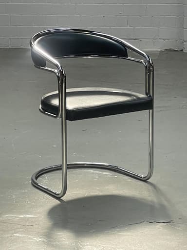 A modern armchair with a tubular metal frame and upholstered seat and backrest. The frame has a chrome finish and features a distinctive cantilevered base. The seat and backrest are padded and covered in black material, likely faux leather or vinyl. The armrests are integrated into the frame. — 3D model