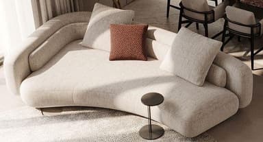 A modern, large, curved sectional sofa upholstered in a light beige textured fabric. It features a low-profile design with integrated, rounded backrests that follow the organic curvature of the piece. The sofa is accessorized with several loose throw pillows in matching and contrasting reddish-brown fabric, contributing to its comfortable and inviting appearance. A small, dark side table is placed near one end. — 3D model