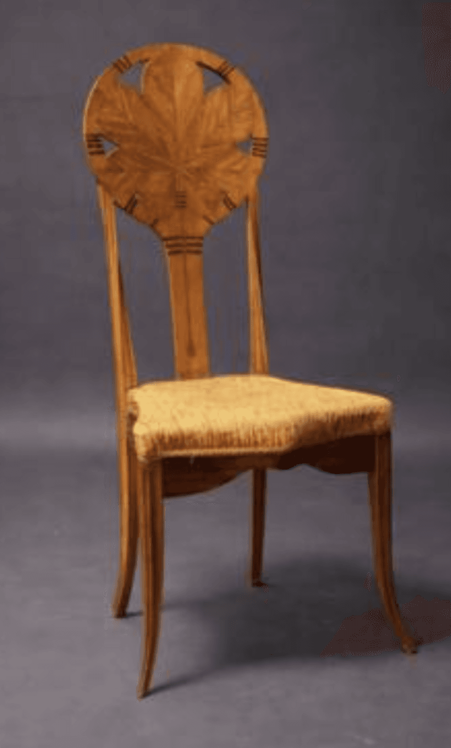 A finely crafted wooden chair with a rounded backrest featuring a carved leaf motif within a circular frame. The seat appears to be upholstered with a woven natural fiber material. The legs are slender and curved, contributing to an elegant and possibly antique aesthetic. — 3D model