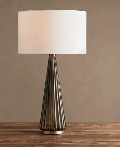 A modern table lamp featuring a conical, fluted base made of smoked glass, accented with brass elements, and topped with a cylindrical white fabric drum shade. — 3D model