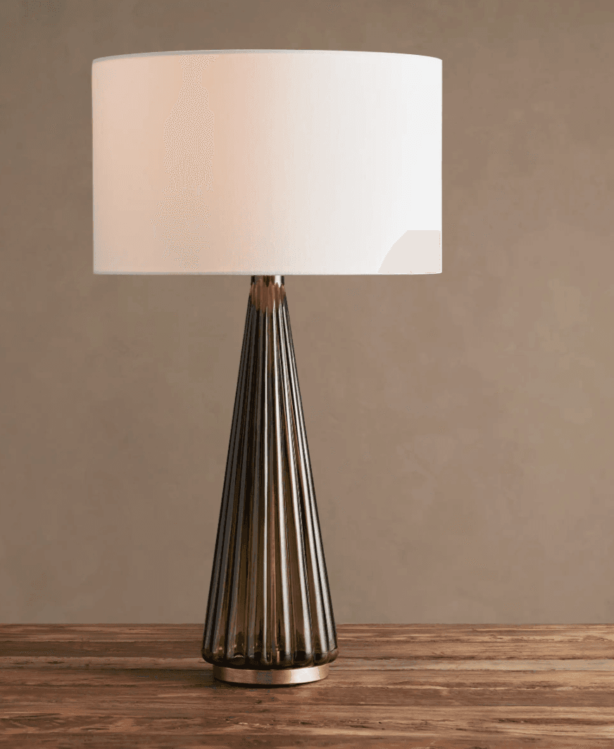 A modern table lamp featuring a conical, fluted base made of smoked glass, accented with brass elements, and topped with a cylindrical white fabric drum shade. — 3D model