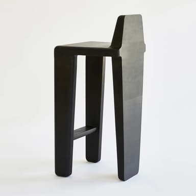 A modern black-stained oak bar stool featuring a minimalist design with an integrated backrest. The stool has a square seat and four robust, slightly tapered legs. A single metal footrest bar connects the front legs. The wood grain is visible beneath the black finish. — 3D model