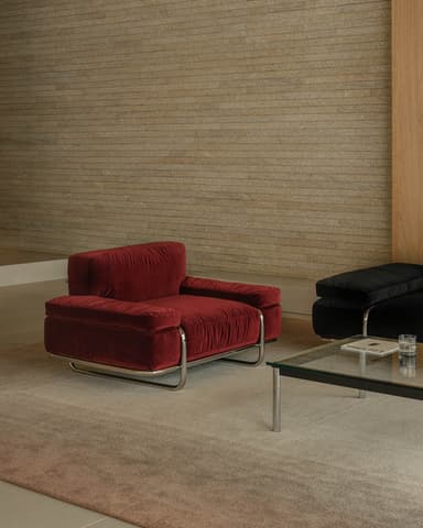 A single-seat armchair with a plush, deep red velvet upholstery. The armchair features a low-profile design with generously padded seat, back, and armrests. It is supported by a sleek, modern chrome metal frame that forms a cantilever base with rounded edges. The upholstery has a subtle tufted texture. — 3D model