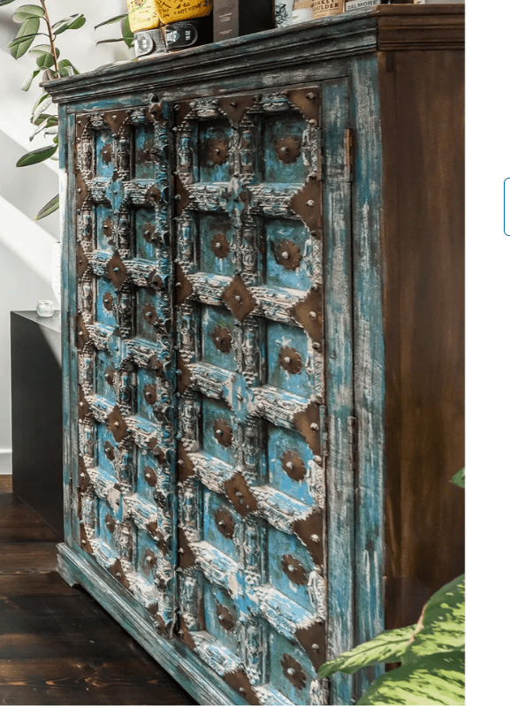 A distressed, carved wooden cabinet with two doors featuring intricate patterns. The doors are adorned with metal decorative elements and have a distressed blue and white finish. The sides of the cabinet appear to be a dark wood. — 3D model
