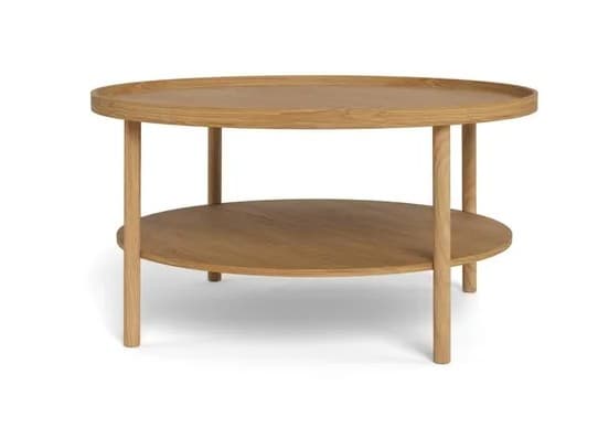 A modern round coffee table crafted from light-toned oak wood, featuring a two-tier design. The top surface has a subtly raised edge, creating a tray-like effect, while a circular lower shelf provides additional storage or display space. The table stands on four sturdy, cylindrical legs. — 3D model