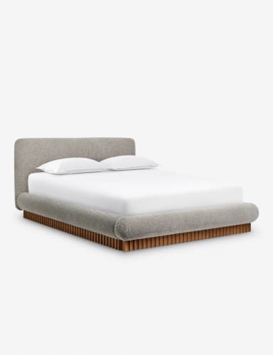 A side profile view of a modern upholstered bed with a curved headboard and a wooden slatted base. The bed frame is upholstered in a textured, light-colored fabric, and it features rounded edges. A white mattress with white bedding and a single white pillow are visible on top. — 3D model