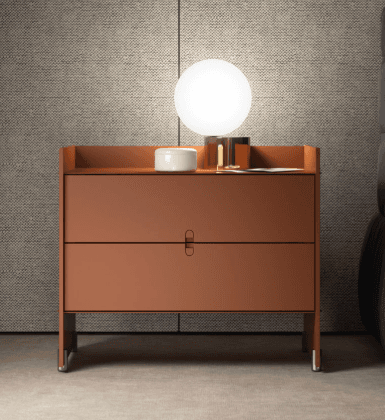 A reddish-brown, modern minimalist nightstand featuring two drawer-like panels on the front, with the upper panel appearing to be a drop-front or door. A subtle, integrated handle is present on the seam between the two panels. The top surface is designed with a raised back and partial sides, creating a shallow tray. The unit rests on two recessed, flat panel legs, each supported by two small, L-shaped metal feet. — 3D model