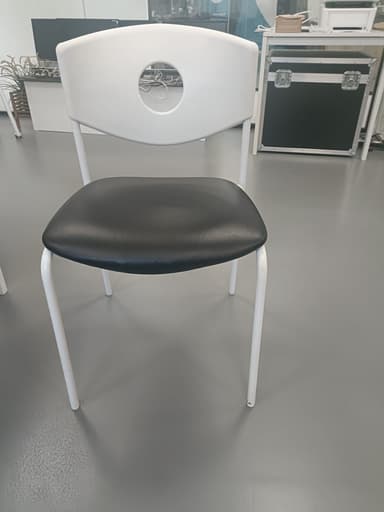 A modern chair with a white, curved backrest featuring a circular cutout. The seat is upholstered in black material, and the frame consists of four slender, white legs. — 3D model