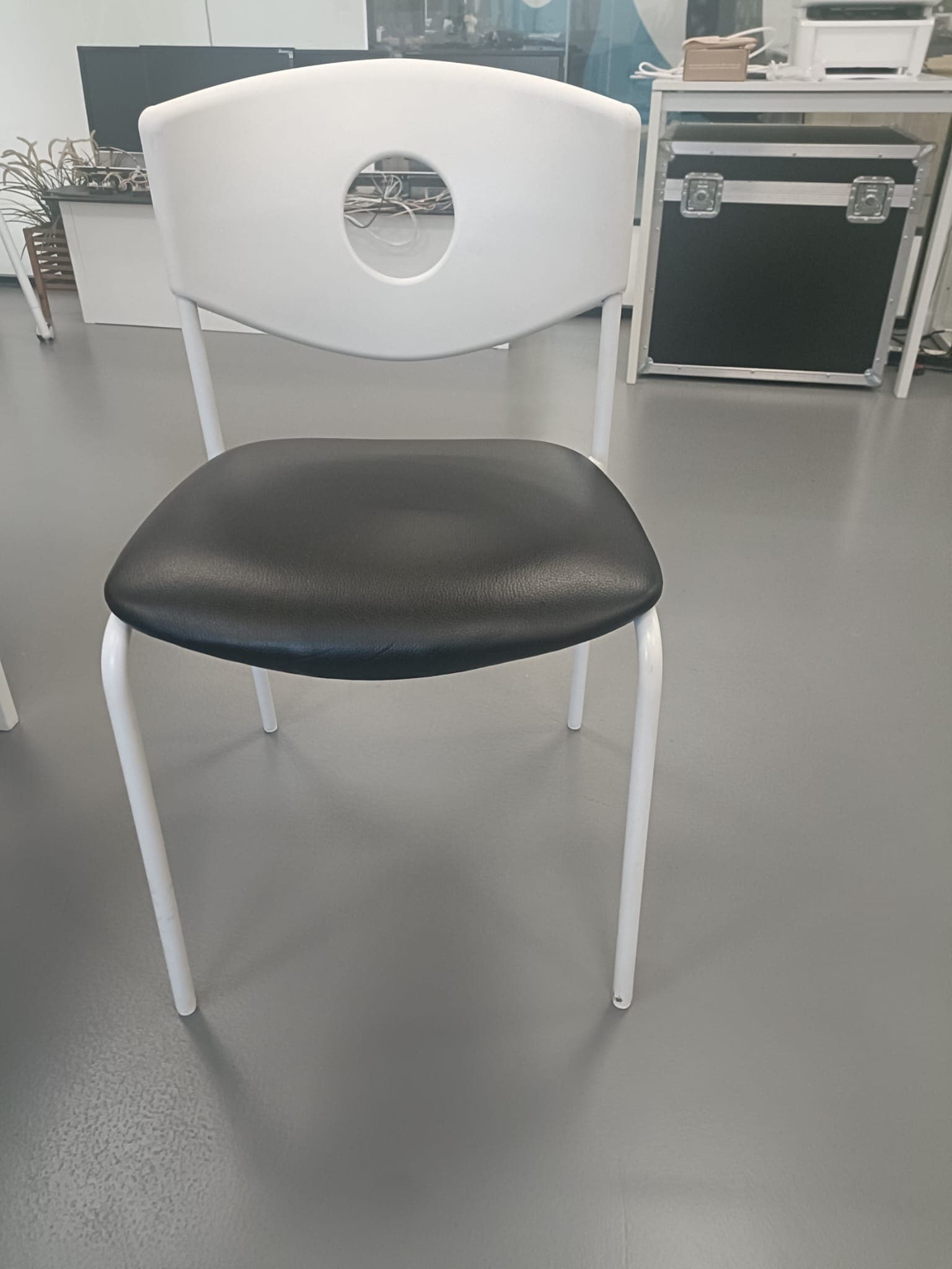 A modern chair with a white, curved backrest featuring a circular cutout. The seat is upholstered in black material, and the frame consists of four slender, white legs. — 3D model