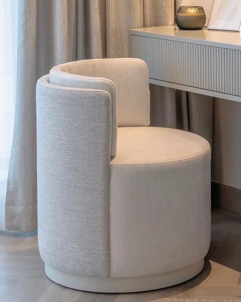 A contemporary barrel lounge chair featuring a fully upholstered, rounded form with a high backrest seamlessly integrating into armrests, covered in a light neutral-toned textile fabric, and resting on a discreet, recessed circular base. — 3D model
