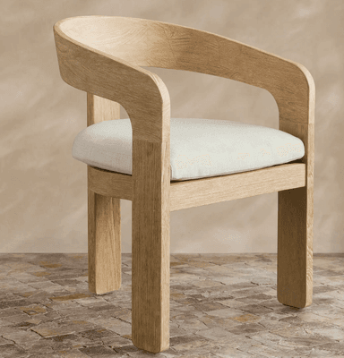 A contemporary dining armchair featuring a solid wood frame with a light, natural finish and visible grain. It has a distinctive curved backrest that seamlessly transitions into integrated armrests. The seat is upholstered with a light-colored, textured fabric cushion. The legs are sturdy and straight, giving the chair a minimalist yet robust appearance. — 3D model