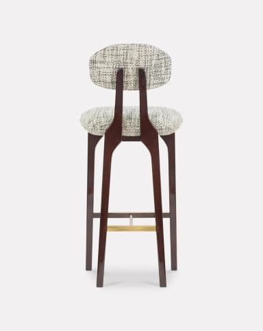 A high-backed bar stool featuring a dark stained wooden frame, a contoured upholstered seat, and a separate, floating upholstered backrest. The frame includes splayed legs and a brass footrest. The upholstery is a textured, patterned fabric in monochrome tones. — 3D model