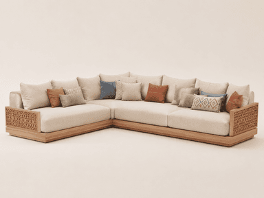 An L-shaped sectional sofa featuring a low-profile natural wood base, intricately woven rattan armrest panels, and plush light-beige fabric cushions, accompanied by an assortment of decorative accent pillows. — 3D model