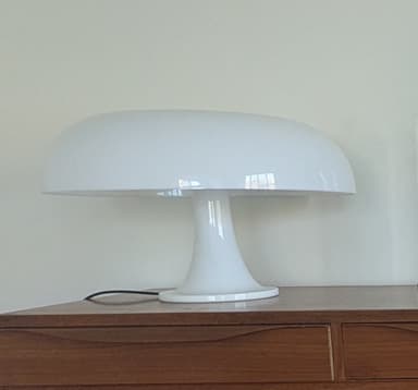 A matte white table lamp with a mushroom-shaped design. The lamp features a domed shade supported by a flared, stem-like base that widens into a circular foot. The overall form is smooth and rounded. — 3D model