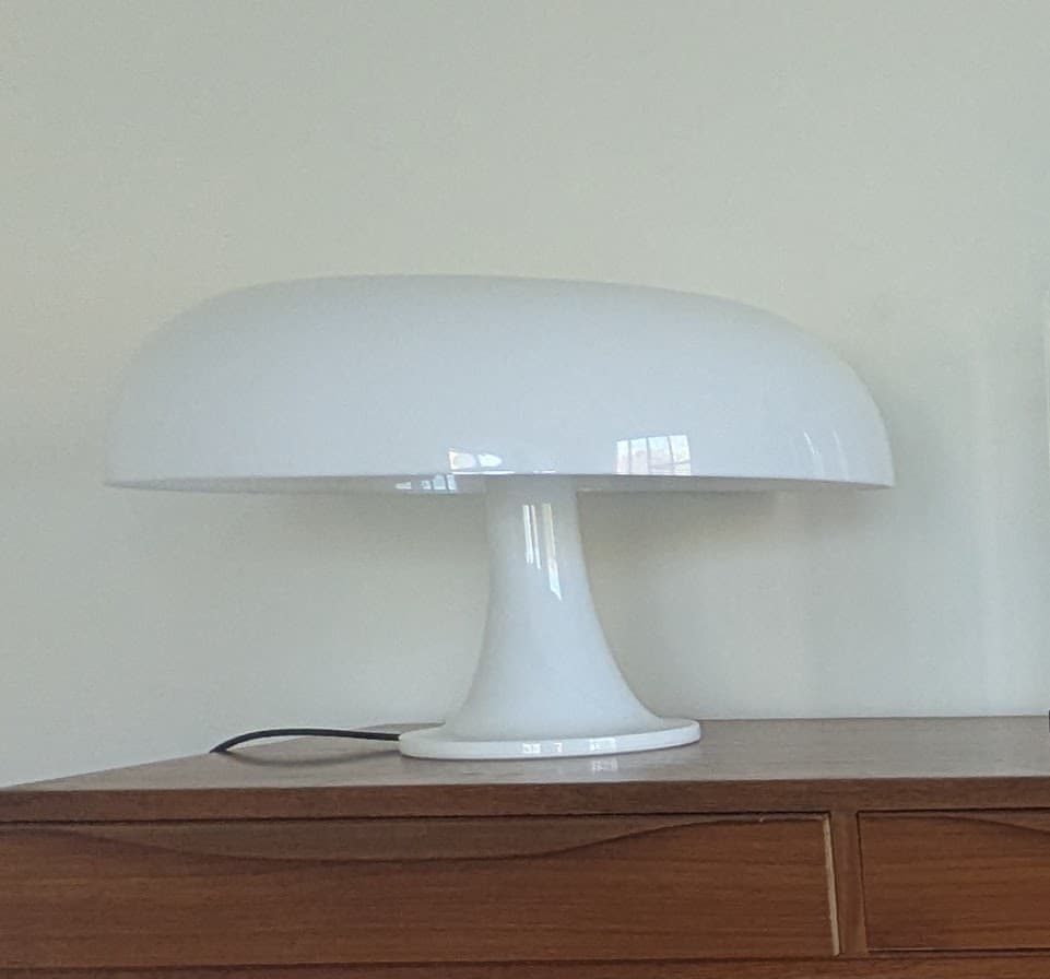 A matte white table lamp with a mushroom-shaped design. The lamp features a domed shade supported by a flared, stem-like base that widens into a circular foot. The overall form is smooth and rounded. — 3D model