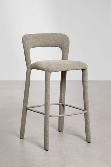 A modern bar stool with a slightly curved backrest and a seat upholstered in a textured beige fabric. The stool has four tapered legs that extend upwards to form the seat and backrest structure. Metal footrests are integrated between the legs. — 3D model